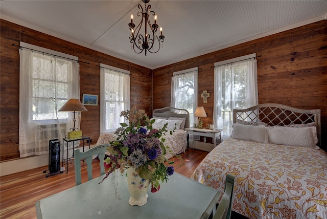 bedroom featuring an inviting chandelier, wooden walls, and hardwood / wood-style floors