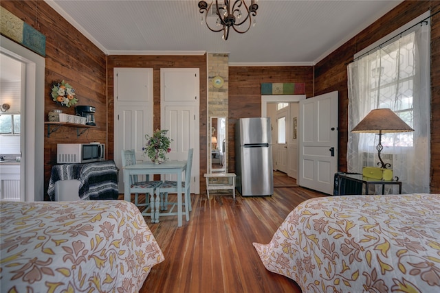 bedroom featuring multiple windows, stainless steel refrigerator, wood walls, and wood-type flooring