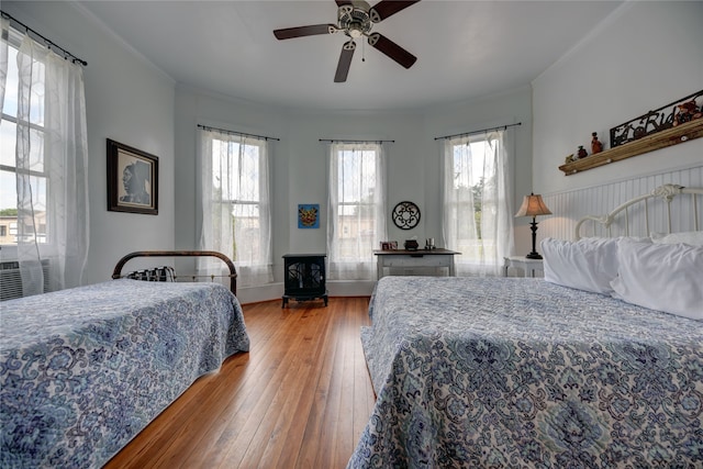 bedroom featuring ornamental molding, wood-type flooring, multiple windows, and ceiling fan