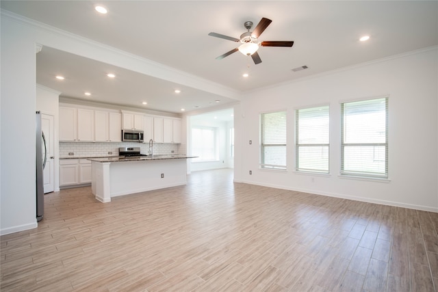 kitchen with ceiling fan, a center island with sink, white cabinetry, appliances with stainless steel finishes, and dark stone counters