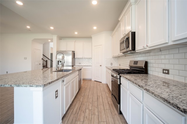 kitchen with stainless steel appliances, white cabinetry, a kitchen island with sink, and sink