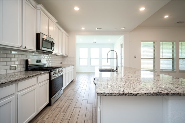 kitchen featuring a healthy amount of sunlight, an island with sink, sink, and stainless steel appliances