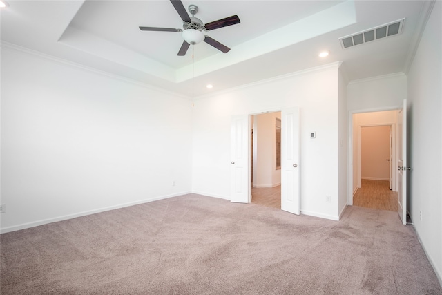 unfurnished bedroom featuring ceiling fan, light colored carpet, a raised ceiling, and crown molding