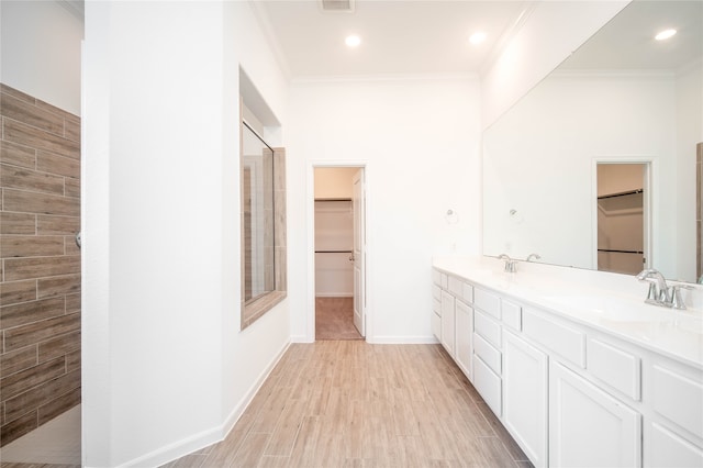 bathroom with wood-type flooring, vanity, ornamental molding, and tiled shower