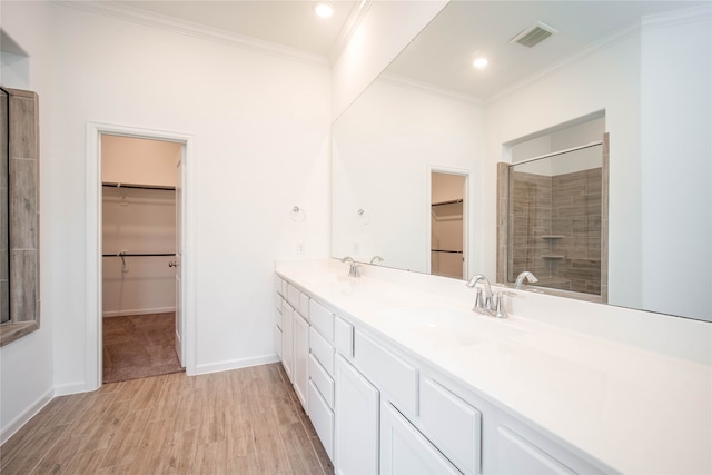 bathroom featuring a tile shower, vanity, wood-type flooring, and ornamental molding