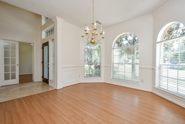 unfurnished room featuring light hardwood / wood-style flooring, a notable chandelier, plenty of natural light, and ornamental molding