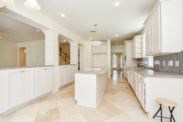 kitchen featuring a center island, sink, white cabinets, decorative backsplash, and ornate columns