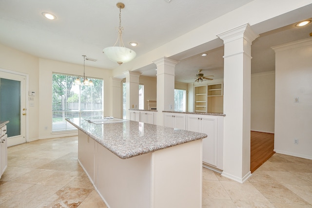 kitchen with ceiling fan with notable chandelier, kitchen peninsula, decorative columns, hanging light fixtures, and a kitchen island