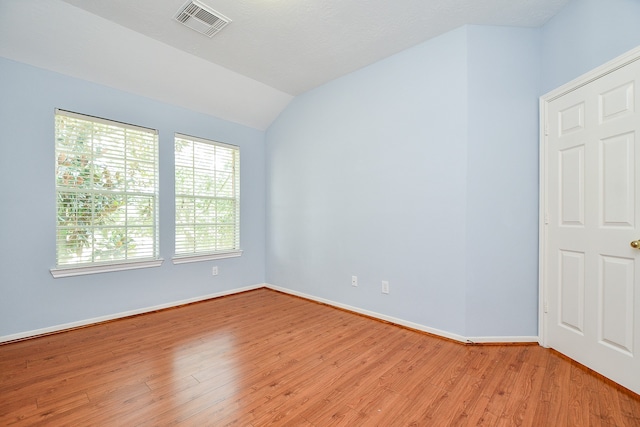 spare room with a textured ceiling, vaulted ceiling, and light hardwood / wood-style flooring