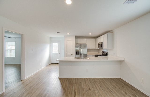 kitchen with light hardwood / wood-style floors, sink, white cabinets, kitchen peninsula, and appliances with stainless steel finishes