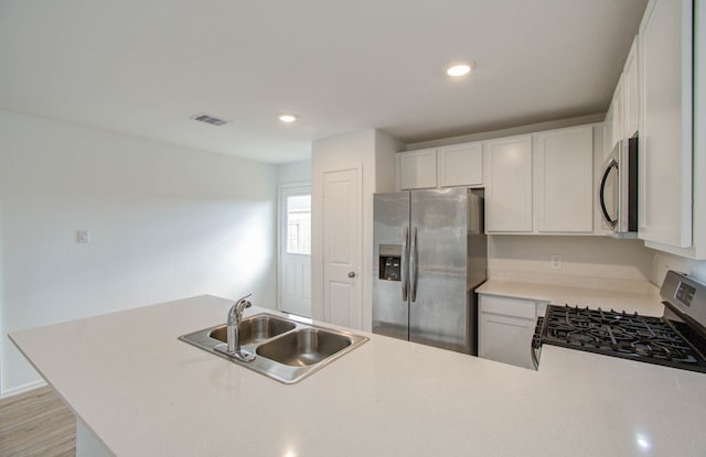 kitchen with appliances with stainless steel finishes, sink, kitchen peninsula, and white cabinetry