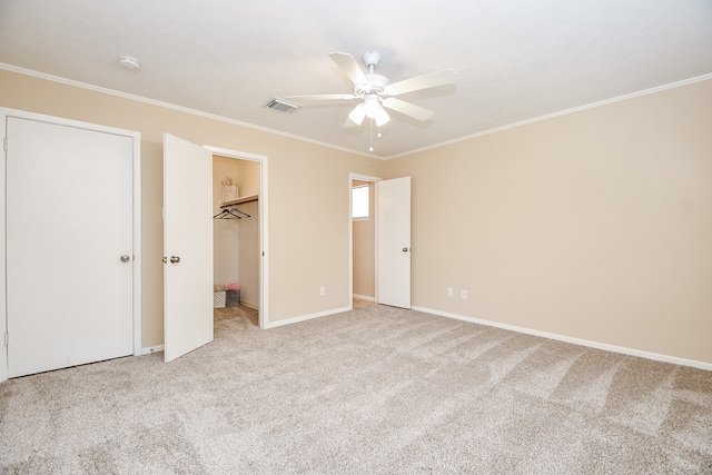 unfurnished bedroom featuring light carpet, crown molding, a spacious closet, and ceiling fan