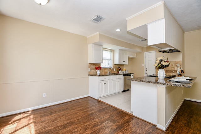 kitchen with kitchen peninsula, white cabinetry, stainless steel dishwasher, dark stone counters, and light hardwood / wood-style flooring