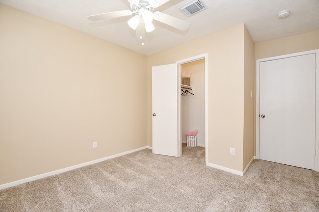 unfurnished bedroom with a closet, ceiling fan, a walk in closet, and light colored carpet