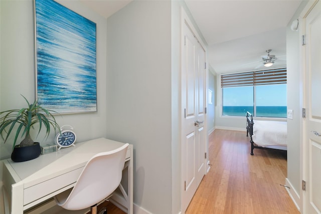 office with a water view, built in desk, ceiling fan, and light hardwood / wood-style flooring