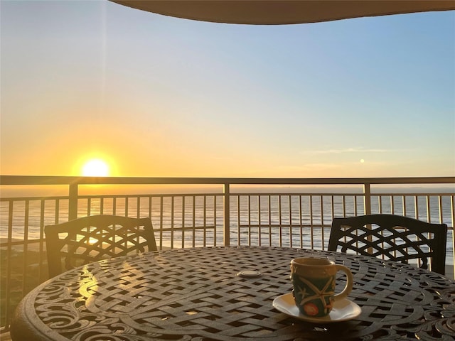 balcony at dusk featuring a water view