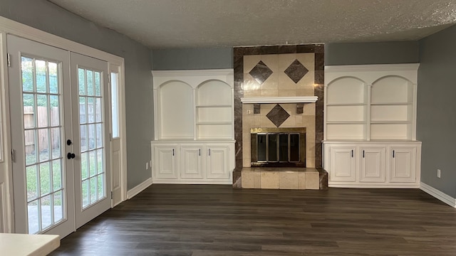 unfurnished living room featuring a tiled fireplace, a textured ceiling, dark hardwood / wood-style floors, built in shelves, and french doors