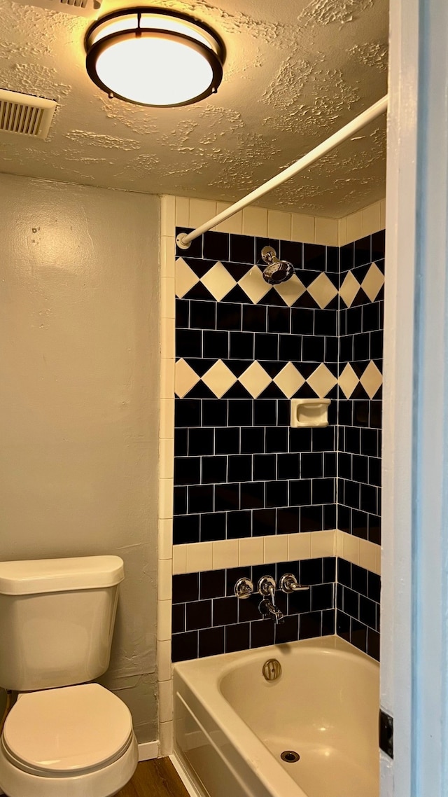 bathroom featuring toilet, tiled shower / bath combo, and a textured ceiling