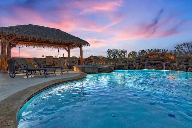 pool at dusk featuring a gazebo, an in ground hot tub, and pool water feature