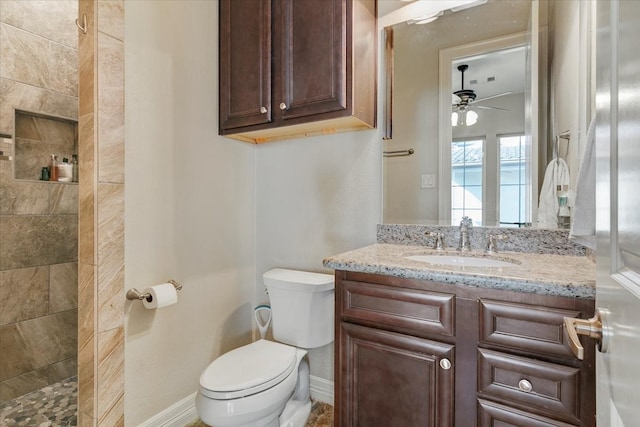 bathroom with a tile shower, vanity, toilet, and ceiling fan