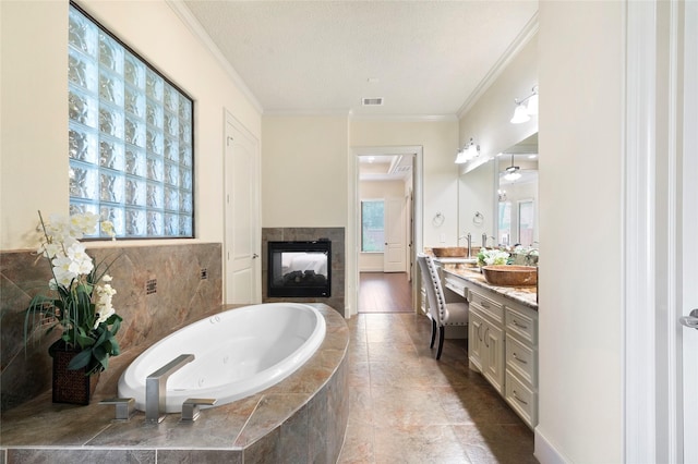 bathroom with crown molding, a textured ceiling, vanity, a tile fireplace, and tiled tub