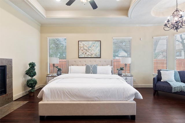 bedroom with dark wood-type flooring, a fireplace, a raised ceiling, and crown molding