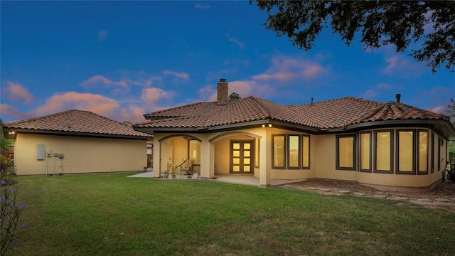 back house at dusk featuring a yard and a patio area