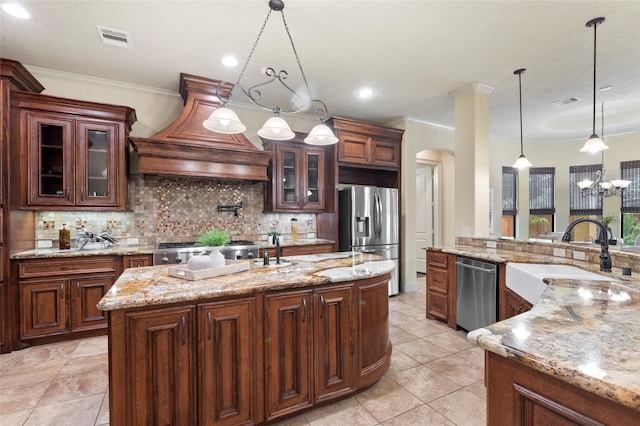 kitchen featuring sink, hanging light fixtures, appliances with stainless steel finishes, custom range hood, and a kitchen island with sink