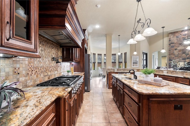 kitchen featuring appliances with stainless steel finishes, decorative light fixtures, an island with sink, sink, and light stone countertops