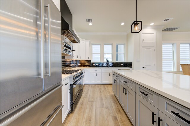 kitchen with ornamental molding, tasteful backsplash, white cabinetry, light stone countertops, and high quality appliances