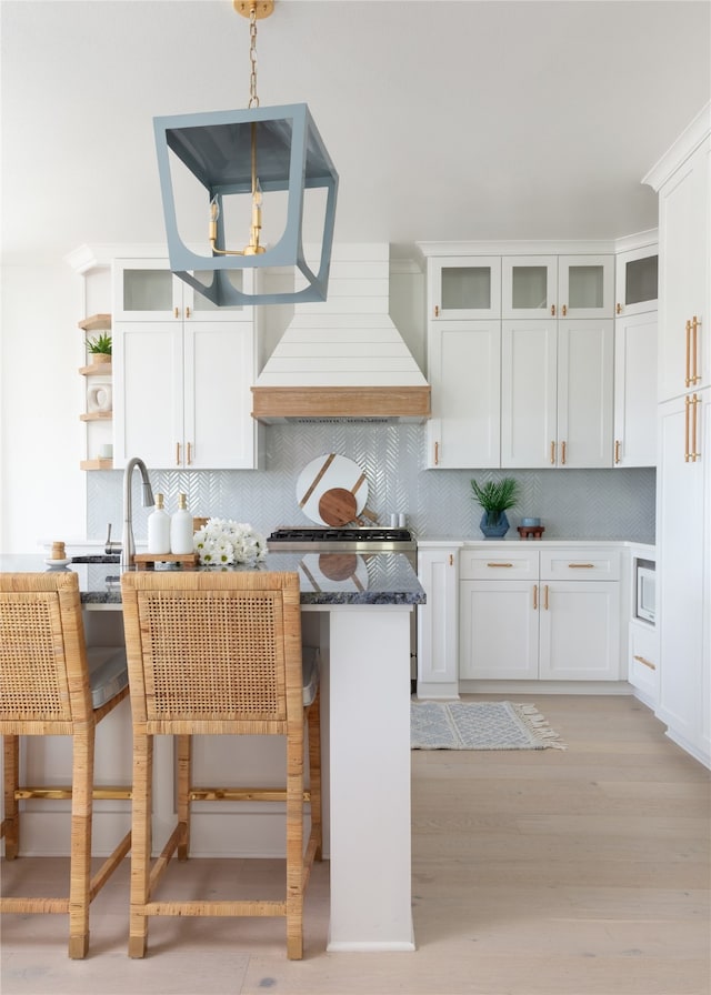 kitchen with pendant lighting, premium range hood, a kitchen bar, and white cabinetry