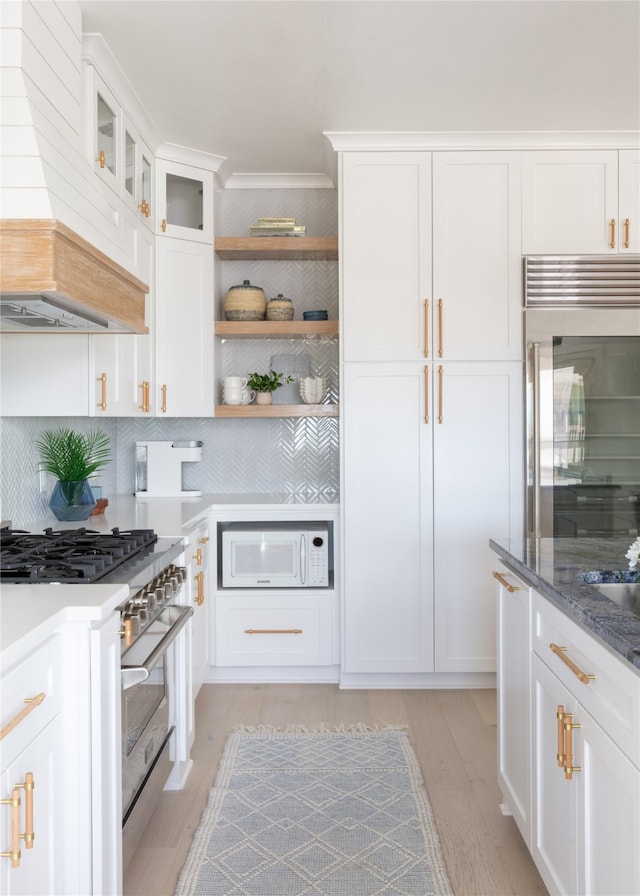 kitchen with white cabinets, premium range hood, light wood-type flooring, backsplash, and high quality appliances