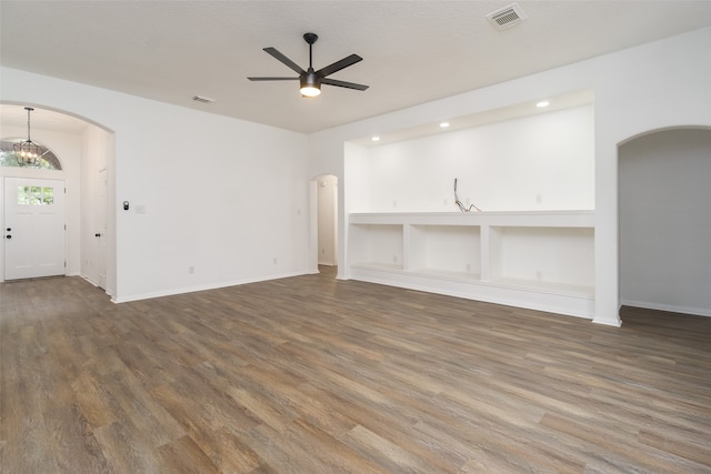 unfurnished living room with ceiling fan with notable chandelier and dark wood-type flooring