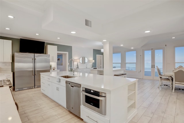 kitchen with light hardwood / wood-style floors, a kitchen island with sink, white cabinets, a water view, and appliances with stainless steel finishes