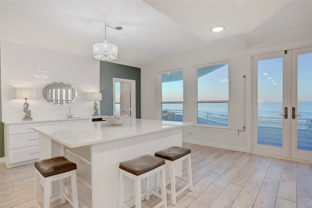 kitchen featuring light hardwood / wood-style floors, white cabinets, a kitchen bar, a water view, and decorative light fixtures