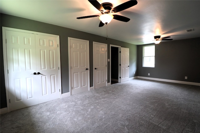 unfurnished bedroom with ceiling fan, multiple closets, and carpet flooring