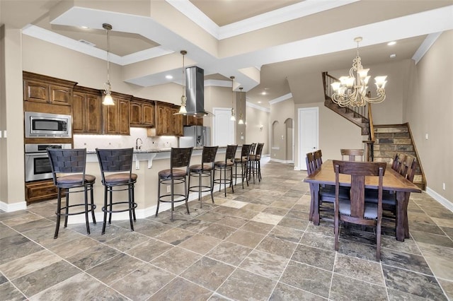 kitchen with an island with sink, a breakfast bar, pendant lighting, island range hood, and appliances with stainless steel finishes