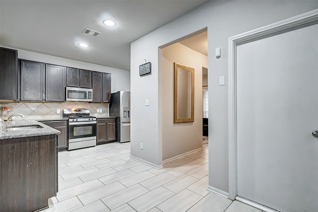 kitchen with backsplash, sink, light stone countertops, dark brown cabinetry, and stainless steel appliances