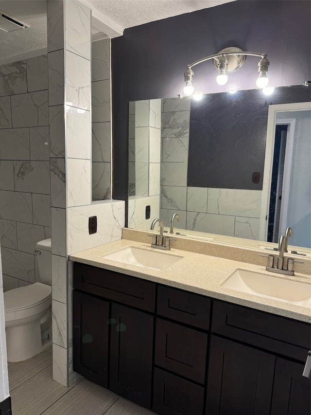 bathroom with a textured ceiling, tile walls, vanity, and toilet