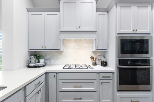 kitchen with gray cabinets, appliances with stainless steel finishes, custom range hood, and tasteful backsplash