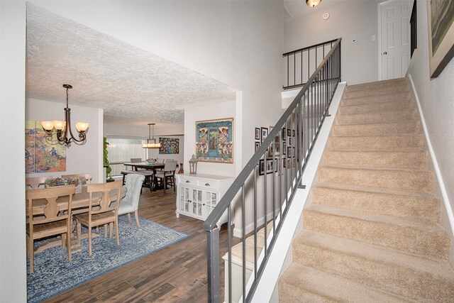 stairs featuring wood-type flooring, a textured ceiling, and a notable chandelier