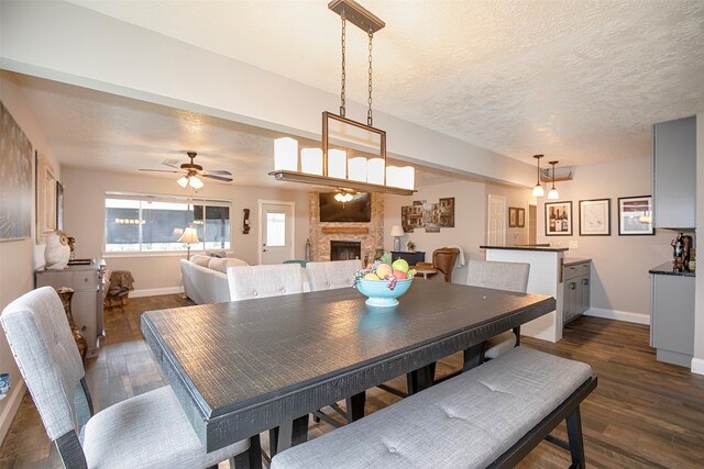 dining room featuring a fireplace, ceiling fan, dark hardwood / wood-style flooring, and a textured ceiling