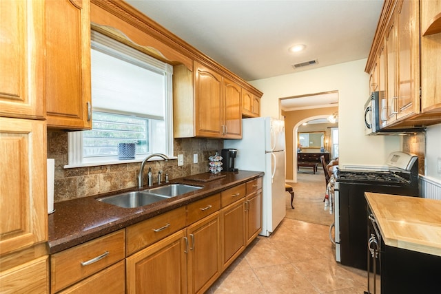 kitchen with sink, light tile patterned floors, appliances with stainless steel finishes, dark stone countertops, and tasteful backsplash