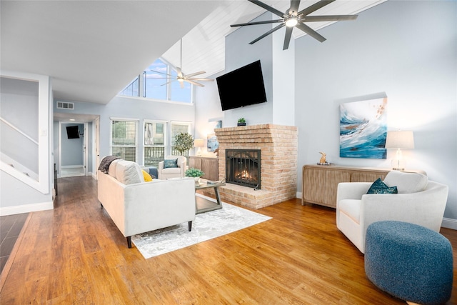 living room featuring high vaulted ceiling, hardwood / wood-style flooring, a brick fireplace, and ceiling fan