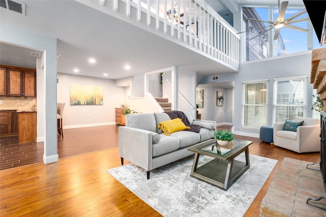 living room featuring wood-type flooring, ceiling fan, and a high ceiling