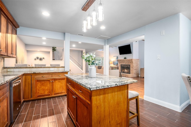 kitchen featuring stainless steel dishwasher, light stone countertops, a fireplace, a kitchen island, and a breakfast bar area