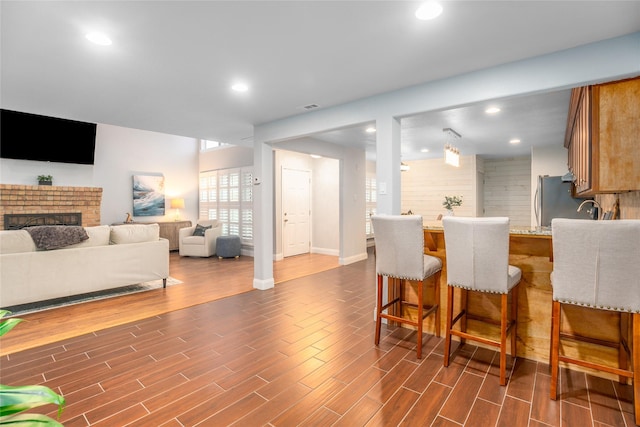 kitchen with stainless steel refrigerator, light stone countertops, a brick fireplace, kitchen peninsula, and a kitchen bar