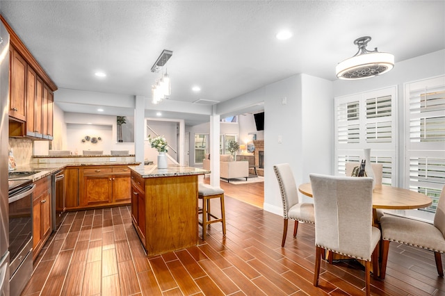 kitchen featuring light stone countertops, stove, tasteful backsplash, a kitchen island, and hanging light fixtures