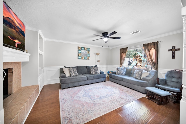 living room with dark wood-type flooring, a tiled fireplace, a textured ceiling, ceiling fan, and ornamental molding