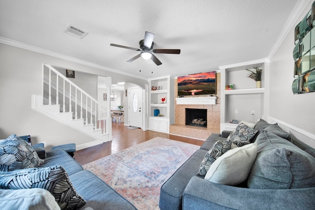 living room featuring ceiling fan, built in features, a fireplace, crown molding, and hardwood / wood-style floors